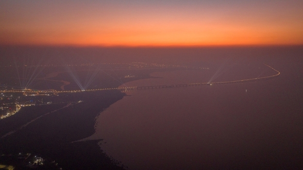 Aerial view of the long bridge spanning across the water at sunset with glowing lights and a vibrant orange sky in Nagda Madhya Pradesh India. Aerial view of the long bridge spanning across the water at sunset with glowing lights and a vibrant orange sky in Nagda Madhya Pradesh India.