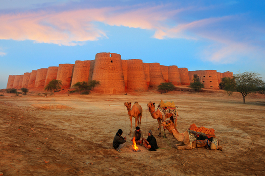 Derawar Punjab Pakistan 31 January 2016 View of Derawar Fort with men sitting around a campfire near camels in the desert landscape.