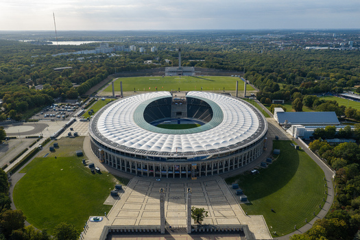 Berlin Berlin Germany 26 September 2026 Aerial view of Olympiastadion Berlin with its iconic circular roof surrounding green parkland and historic architecture under a clear sky.