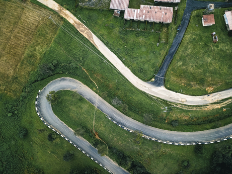 Aerial view of a winding asphalt road snaking through vibrant green fields contrasting with the muted tones of nearby rooftops Obudu Cross River Nigeria.