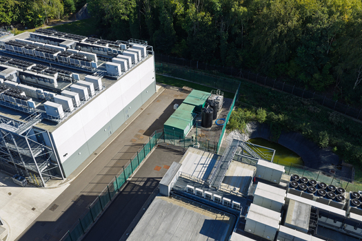 Aerial view of a modern data center facility featuring rooftop cooling units fenced perimeter and surrounding greenery in the United Kingdom.