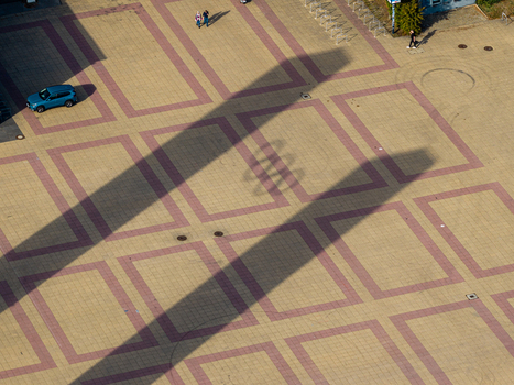 Berlin Berlin Germany 26 September 2026 Aerial view of the paved plaza at Olympiastadion Berlin with long shadows of the Olympic Rings geometric patterns a blue car and people walking.