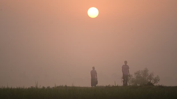 View of people walking in a foggy field at sunrise in Bangladesh.