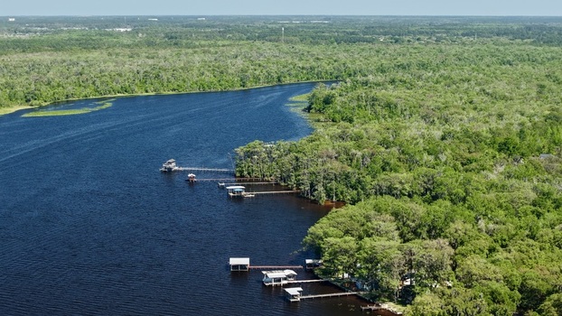 Aerial view of Sixmile Creek with wooden docks extending into the dark blue water surrounded by dense green forest in St. Johns County Florida United States.