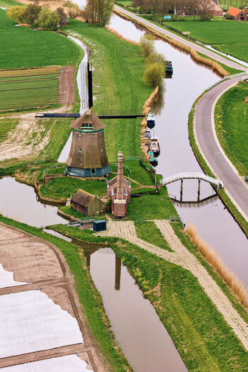 Aerial view of De Kaagmolen windmill and a historic pumping station along a winding canal with green fields and a white bridge in Spanbroek North Holland Netherlands. Aerial view of De Kaagmolen windmill and a historic pumping station along a winding canal with green fields and a white bridge in Spanbroek North Holland Netherlands.