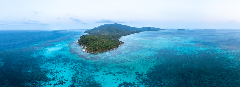 Aerial view of Pantai Ujung Gelam featuring a lush tropical island surrounded by vibrant turquoise coral reefs and clear blue water in Karimunjawa Central Java Indonesia. Aerial view of Pantai Ujung Gelam featuring a lush tropical island surrounded by vibrant turquoise coral reefs and clear blue water in Karimunjawa Central Java Indonesia.