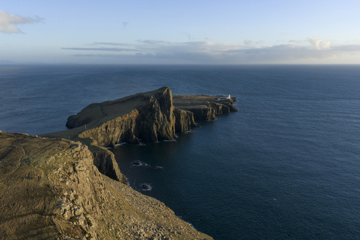 Aerial view of Neist Point Lighthouse on the edge of dramatic cliffs overlooking the blue waters of the Atlantic Ocean under a clear sky Isle of Skye Scotland United Kingdom. Aerial view of Neist Point Lighthouse on the edge of dramatic cliffs overlooking the blue waters of the Atlantic Ocean under a clear sky Isle of Skye Scotland United Kingdom.