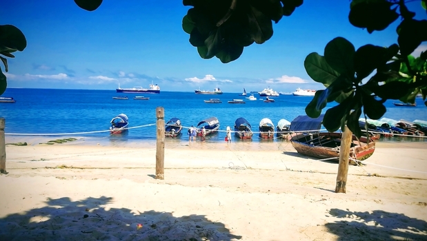 View of traditional wooden boats moored on the sandy beach with the blue ocean and distant ships under a clear sky in Zanzibar Mjini Magharibi Regio Tanzania. View of traditional wooden boats moored on the sandy beach with the blue ocean and distant ships under a clear sky in Zanzibar Mjini Magharibi Regio Tanzania.