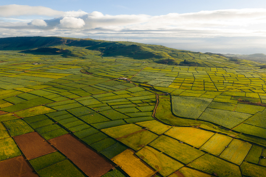 Aerial view of Pico Dona Joana with a patchwork of agricultural fields rolling green hills and wind turbines under a cloudy sky in Feteira Acores Portugal. Aerial view of Pico Dona Joana with a patchwork of agricultural fields rolling green hills and wind turbines under a cloudy sky in Feteira Acores Portugal.