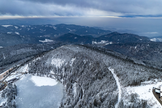 Aerial view of the frozen Mummelsee lake surrounded by snow covered pine forests and the Black Forest mountains in Seebach Baden Wurttemberg Germany. Aerial view of the frozen Mummelsee lake surrounded by snow covered pine forests and the Black Forest mountains in Seebach Baden Wurttemberg Germany.