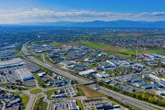 Aerial view of sprawling industrial buildings juxtaposed against verdant fields with the distant Alps painted against the horizon Sausheim Grand Est France.