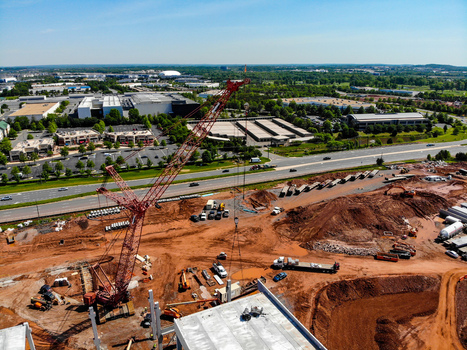 Aerial view of a large red crane at a construction site with red soil concrete foundations and surrounding commercial buildings in Ashburn Virginia United States. Aerial view of a large red crane at a construction site with red soil concrete foundations and surrounding commercial buildings in Ashburn Virginia United States.