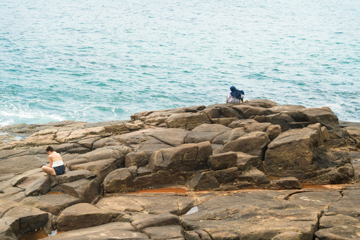 View of people sitting on large coastal rocks overlooking the turquoise ocean in Mirissa Southern Province Sri Lanka. View of people sitting on large coastal rocks overlooking the turquoise ocean in Mirissa Southern Province Sri Lanka.