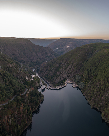 Aerial view of Encoro de Santo Estevo dam nestled in a deep river valley surrounded by lush green hills and dense forests at sunset in Ourense Ourense Spain. Aerial view of Encoro de Santo Estevo dam nestled in a deep river valley surrounded by lush green hills and dense forests at sunset in Ourense Ourense Spain.