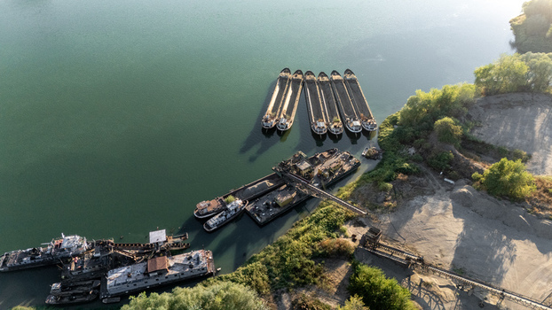 Aerial view of barges docked on the Sava River near the industrial port facilities with gravel piles and lush greenery in Sremska Mitrovica Vojvodina Serbia.