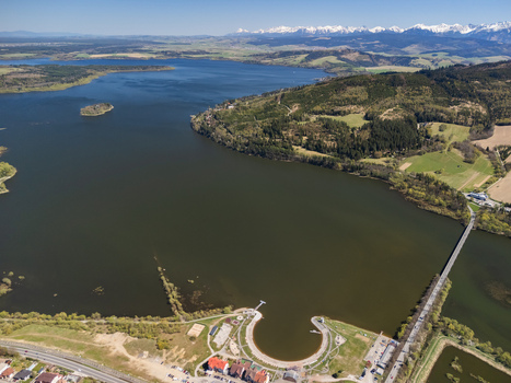 Aerial view of Oravska priehrada reservoir with a long bridge lush green hills and snow capped mountains in Namestovo Zilinsky kraj Slovakia. Aerial view of Oravska priehrada reservoir with a long bridge lush green hills and snow capped mountains in Namestovo Zilinsky kraj Slovakia.