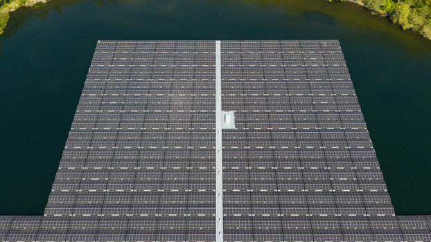 Aerial view of a large floating solar farm with rows of photovoltaic panels on a calm lake surrounded by green trees in Zwolle Overijssel Netherlands. Aerial view of a large floating solar farm with rows of photovoltaic panels on a calm lake surrounded by green trees in Zwolle Overijssel Netherlands.