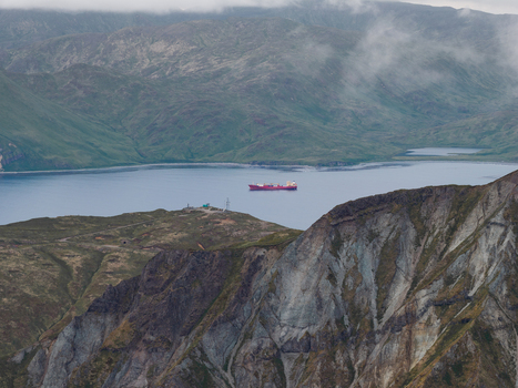 Aerial view of a cargo ship sailing in the calm waters of a bay surrounded by rugged mountains and misty slopes in Unalaska Alaska United States.