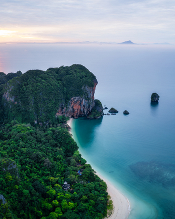 Aerial view of Railay Beach featuring towering limestone cliffs lush tropical forest white sand and turquoise water along the coast in Ao Nang Krabi Thailand. Aerial view of Railay Beach featuring towering limestone cliffs lush tropical forest white sand and turquoise water along the coast in Ao Nang Krabi Thailand.