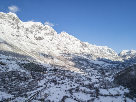 Aerial view of the snow covered village nestled in the Accursed Mountains with winding roads and pine trees in Boge Shkoder County Albania. Aerial view of the snow covered village nestled in the Accursed Mountains with winding roads and pine trees in Boge Shkoder County Albania.