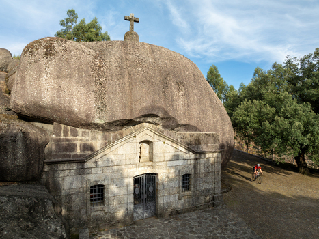 Aerial view of Santuario de Nossa Senhora da Lapa a stone chapel built under a giant boulder with a cross on top and a cyclist on a nearby path Soutelo Braga Portugal. Aerial view of Santuario de Nossa Senhora da Lapa a stone chapel built under a giant boulder with a cross on top and a cyclist on a nearby path Soutelo Braga Portugal.