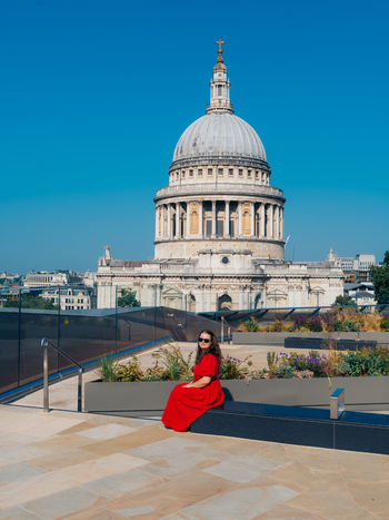 View of a woman in vivid red on a modern terrace grand St Paul s Cathedral dome under a clear blue sky London England United Kingdom. View of a woman in vivid red on a modern terrace grand St Paul s Cathedral dome under a clear blue sky London England United Kingdom.