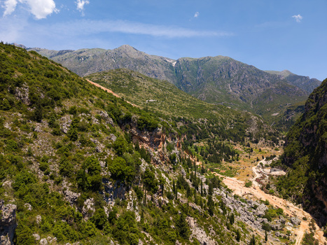 Aerial view of the rugged Gjipe Canyon with steep green slopes rocky cliffs and a winding path leading through the valley towards mountains in Dhermi Vlore County Albania.