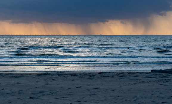 View of the Strand Wijk aan Zee beach with waves crashing under a dramatic sky and rain falling over the sea in Wijk aan Zee North Holland Netherlands. View of the Strand Wijk aan Zee beach with waves crashing under a dramatic sky and rain falling over the sea in Wijk aan Zee North Holland Netherlands.