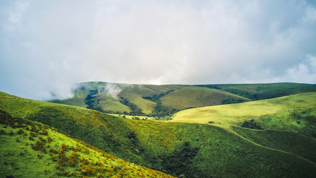 Aerial view of lush emerald slopes and dramatic velvet green hills partially shrouded in ethereal mist under a dramatic cloudy sky Obudu Cross River Nigeria.