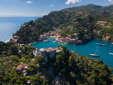 Aerial view of the colorful harbor with boats anchored in turquoise water and Castello Brown on a lush green hill in Portofino Liguria Italy.