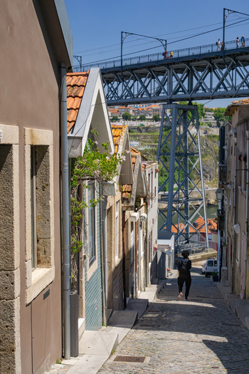 Porto Portugal 13 July 2021 View of a narrow street leading towards the Dom Luís I Bridge where the warm tones of the buildings contrast with the cool steel of the bridge. Porto Portugal 13 July 2021 View of a narrow street leading towards the Dom Luís I Bridge where the warm tones of the buildings contrast with the cool steel of the bridge.