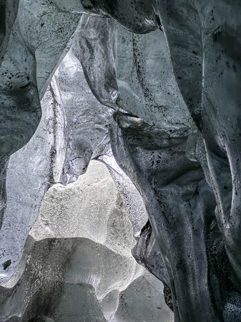 View of the interior of a glacier ice cave with translucent blue ice walls and textured frozen surfaces in Iceland. View of the interior of a glacier ice cave with translucent blue ice walls and textured frozen surfaces in Iceland.