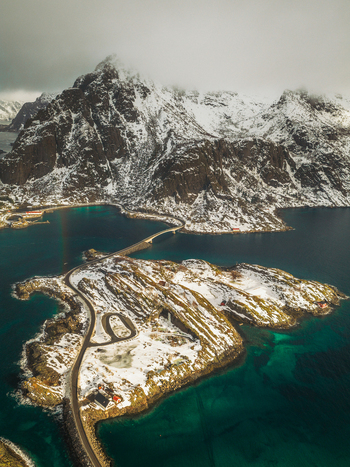 Aerial view of snow dusted islands connected by winding roads beneath towering frosted mountains Henningsv&aelig;r Nordland Norway.