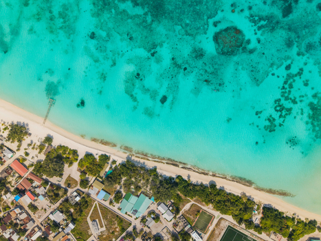 Aerial view of the turquoise sea meeting the sandy beach and the small island buildings Vashafaru Island Thiladhummathi Atoll Maldives.