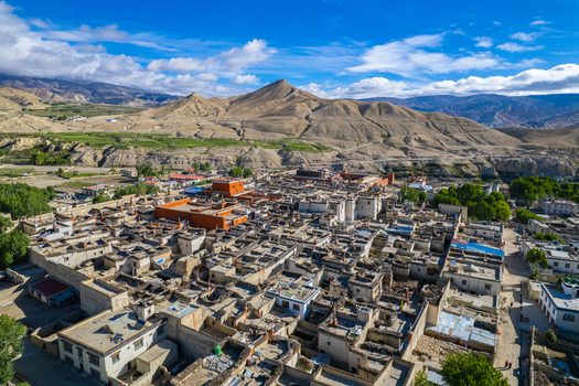 Aerial view of the historic town of Lo Manthang with traditional stone houses a prominent red monastery and prayer flags set against the arid mountain landscape of Nepal.