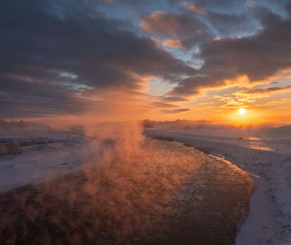 Aerial view of Lielupe river at sunrise with mist rising from the water over snow covered banks in Ziedoni Bauska Municipality Latvia.