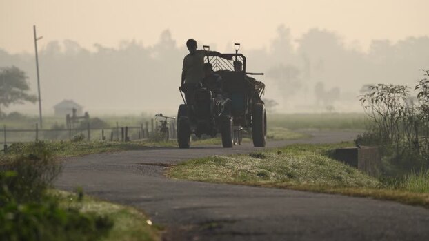 View of people on a tractor on a misty rural road Bangladesh.