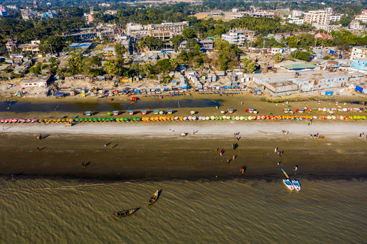 Aerial view of Kuakata beach with rows of colorful umbrellas small wooden boats on the sand and the coastal town in the background in Kuakata Barisal Division Bangladesh. Aerial view of Kuakata beach with rows of colorful umbrellas small wooden boats on the sand and the coastal town in the background in Kuakata Barisal Division Bangladesh.