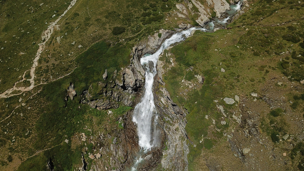 Aerial view of cascading waterfall carving through rugged terrain a symphony of white water against the lush green and brown slopes Valgrisenche Aosta Valley Italy.
