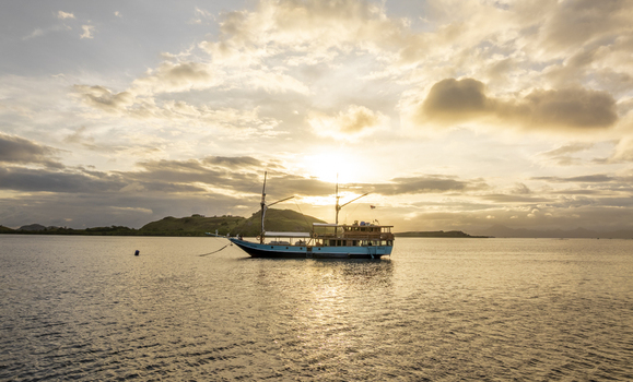 Aerial view of a traditional wooden phinisi boat anchored in calm waters off Komodo Island at sunset with golden light reflecting on the sea Komodo East Nusa Tenggara Indonesia.