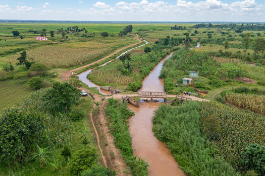 Aerial view of a river flowing through agricultural fields with a small bridge and lush greenery in the rural landscape of Butaleja Eastern Region Uganda. Aerial view of a river flowing through agricultural fields with a small bridge and lush greenery in the rural landscape of Butaleja Eastern Region Uganda.