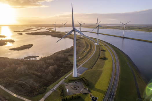 Aerial view of wind turbines standing along a dike next to a lake during a golden sunset with reflections on the water in the Netherlands. Aerial view of wind turbines standing along a dike next to a lake during a golden sunset with reflections on the water in the Netherlands.