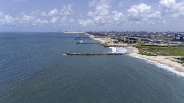 Aerial view of the coastline featuring stone groynes sandy beaches and the urban skyline along Lekki Beach Road under a cloudy sky in Lekki Lagos Nigeria. Aerial view of the coastline featuring stone groynes sandy beaches and the urban skyline along Lekki Beach Road under a cloudy sky in Lekki Lagos Nigeria.