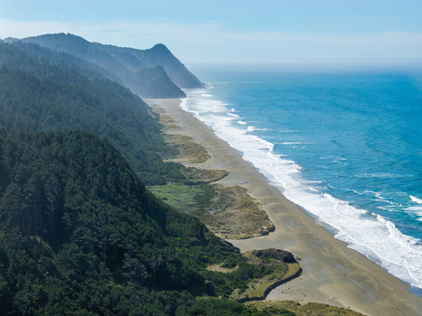 Aerial view of the rugged coastline along Highway 101 in southern Oregon featuring dense evergreen forests meeting the sandy beach and the Pacific Ocean Gold Beach Oregon United States. Aerial view of the rugged coastline along Highway 101 in southern Oregon featuring dense evergreen forests meeting the sandy beach and the Pacific Ocean Gold Beach Oregon United States.