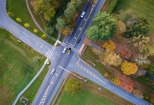 Aerial view of a road intersection surrounded by autumn trees and green fields with cars driving on the asphalt roads in Hyde Park New York United States.