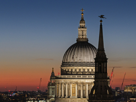 Aerial view of St. Paul s Cathedral with its iconic dome and spires illuminated against a sunset sky overlooking the city skyline London England United Kingdom.