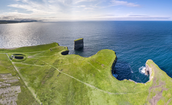 Aerial view of Dun Briste sea stack rising from the Atlantic Ocean near the green grassy cliffs of the coastline in County Mayo Ireland. Aerial view of Dun Briste sea stack rising from the Atlantic Ocean near the green grassy cliffs of the coastline in County Mayo Ireland.