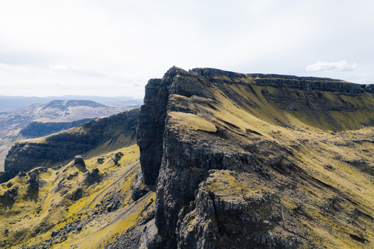 Aerial view of The Storr a dramatic basalt rock formation with rugged cliffs and grassy slopes under a bright sky Portree Scotland United Kingdom. Aerial view of The Storr a dramatic basalt rock formation with rugged cliffs and grassy slopes under a bright sky Portree Scotland United Kingdom.