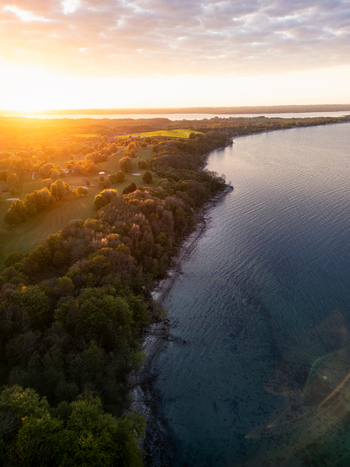 Aerial view of Bockholmwik coastline with lush green trees and calm waters under a golden sunset sky in Munkbrarup Schleswig Holstein Germany.