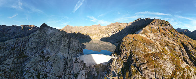 Aerial view of the Vieux Emosson Dam and lake surrounded by rugged alpine mountains and rocky terrain under a clear blue sky in Finhaut Valais Switzerland. Aerial view of the Vieux Emosson Dam and lake surrounded by rugged alpine mountains and rocky terrain under a clear blue sky in Finhaut Valais Switzerland.
